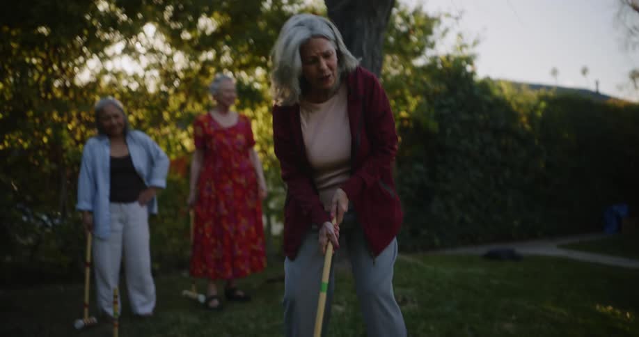 Three elderly women in the backyard playing croquet