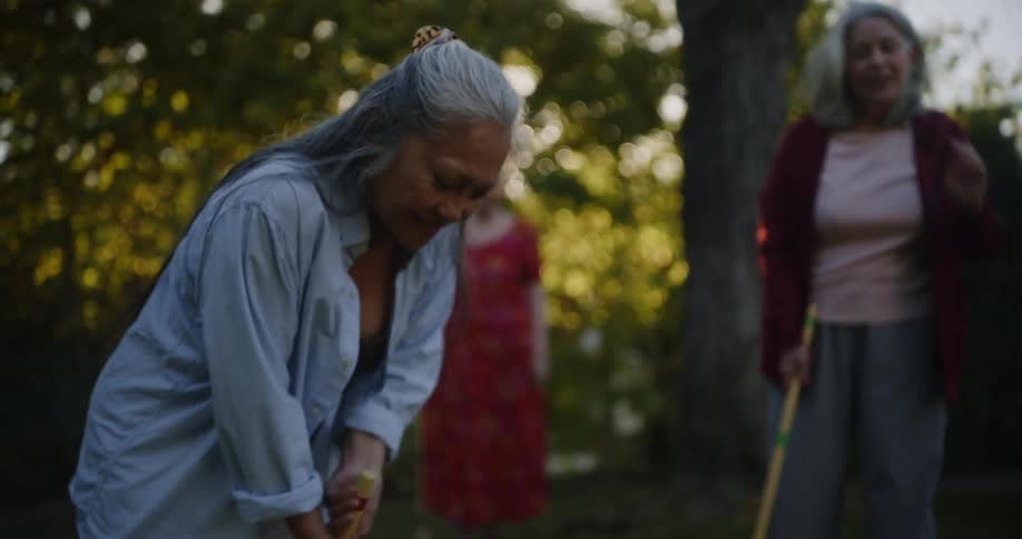 Three adult female friends playing croquet in the backyard