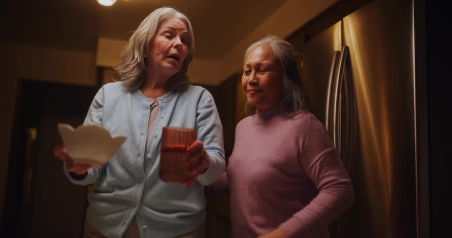 Two female friends share a laugh as they clean the kitchen