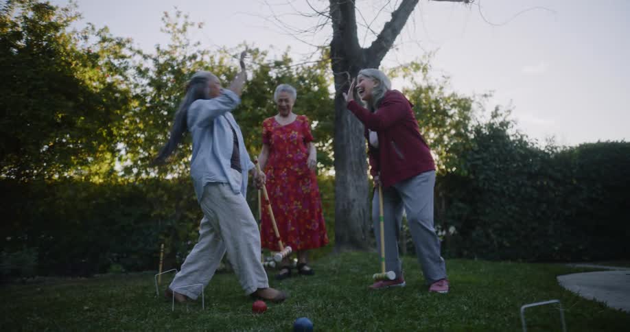 Three women laugh while playing croquet