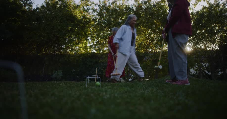 Older female friends play a game of croquet in a yard