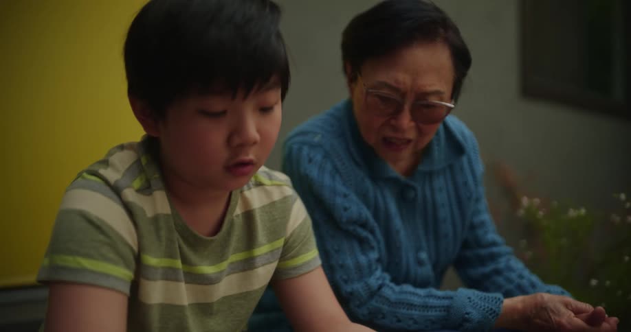 A woman and her grandson sit outside as he plays a video game