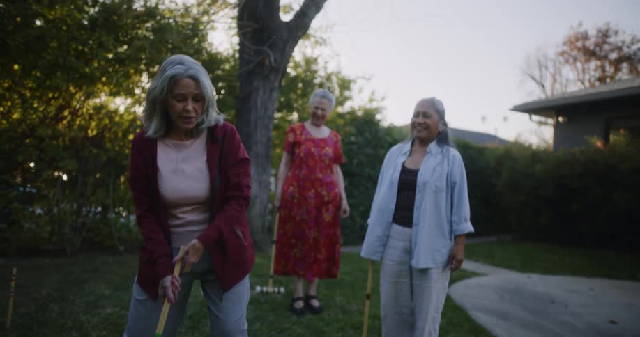 Three women play croquet in a yard