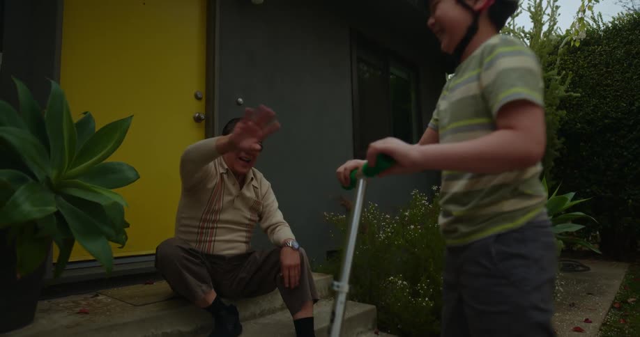 A grandfather watches his grandson ride a scooter