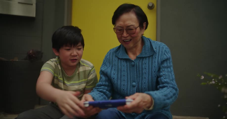 A boy is showing and older woman how to play a handheld game