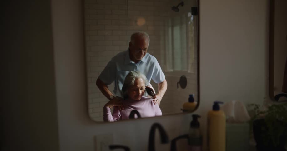 Reflection in mirror of an elderly husband lovingly brushing his wifes hair