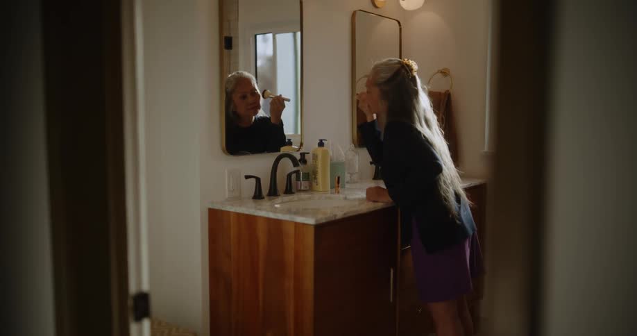 Elderly lady in the bathroom in front of the mirror putting on makeup like blush and lipstick