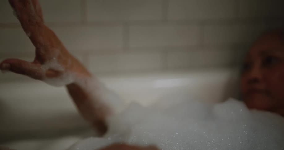 Older woman relaxing in a bubble bath admiring her hands