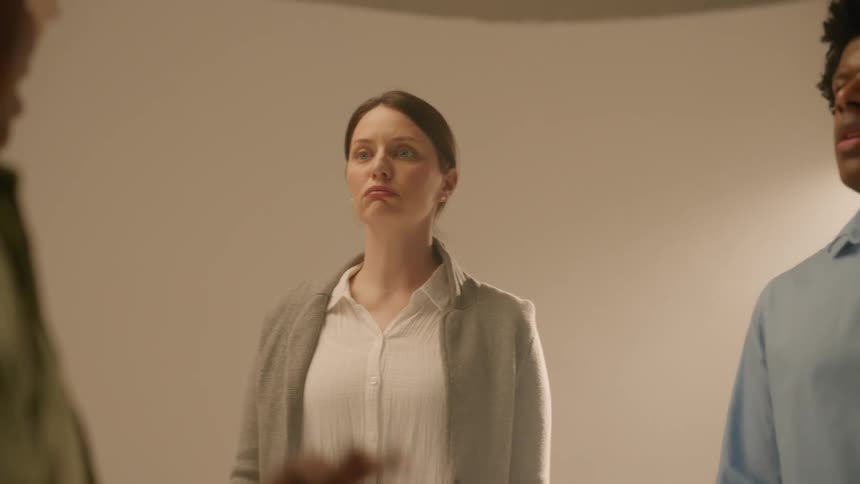 Woman gesturing with her arms and talking to a man and a woman who are concentrated listening inside a recording studio
