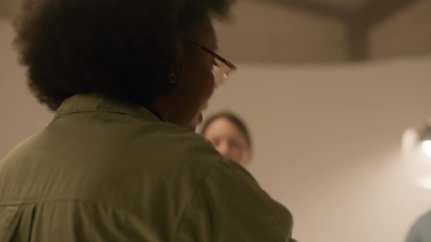 Woman talking to two people in front of her and gesturing with her fingers while they are in a studio