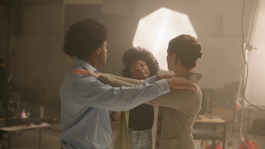 Actors rehearsing in a studio with their arms on each others shoulders with the help of a woman
