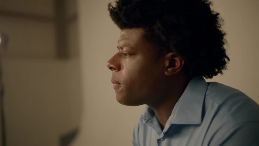 A black man sits in a room listening to someone else speak
