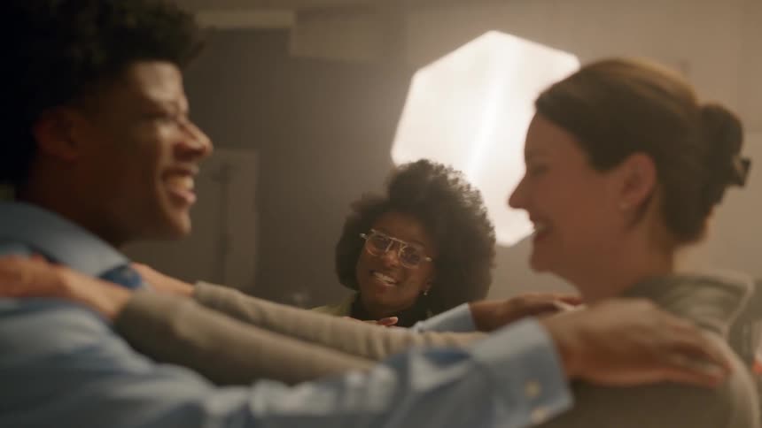 Man and woman with their hands placed on each others shoulders and another smiling woman next to them talking to them in a studio