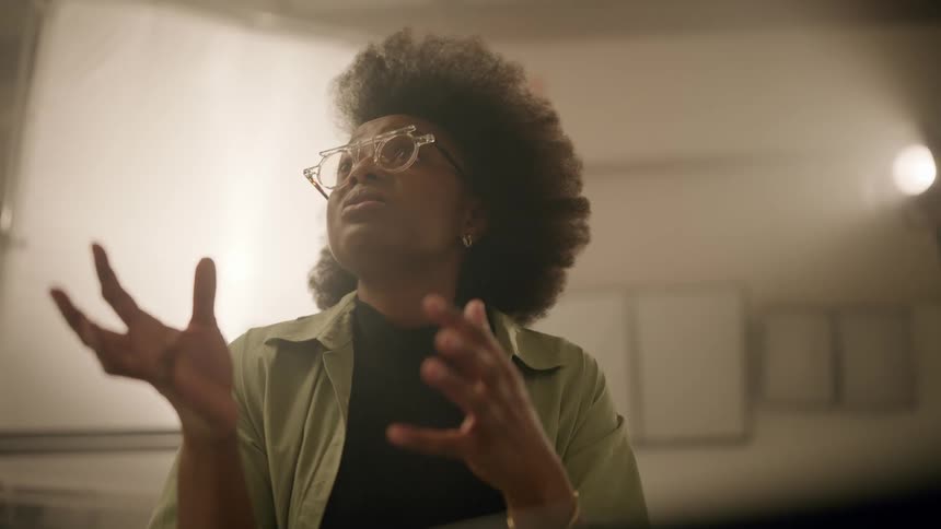 Portrait of a woman with glasses talking and gesturing with her hands while indoors with studio lighting