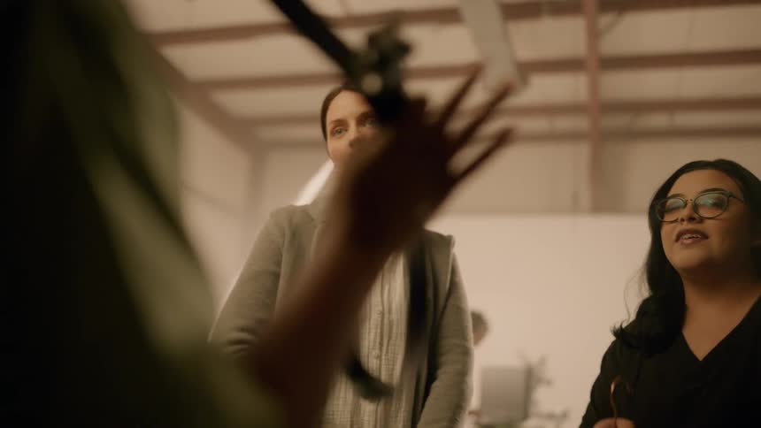 Three women inside a studio talking while one of them holds a hanger with clothes