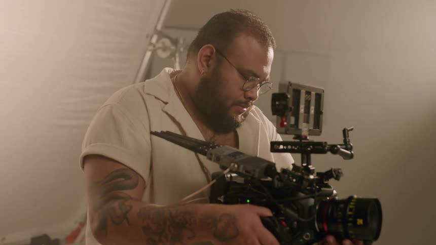 Filmmaker man making a sign with his hands and concentrating with his professional video camera inside a studio