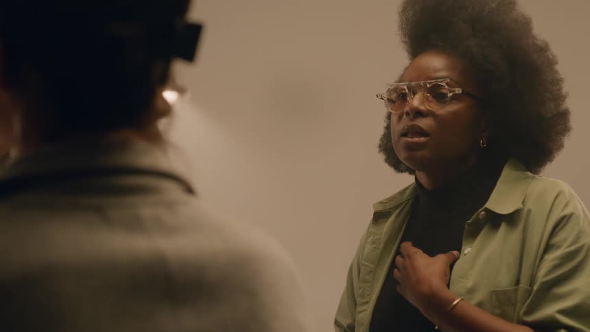 Woman talking and gesturing with her hands to another woman who is having makeup done while they are in a studio