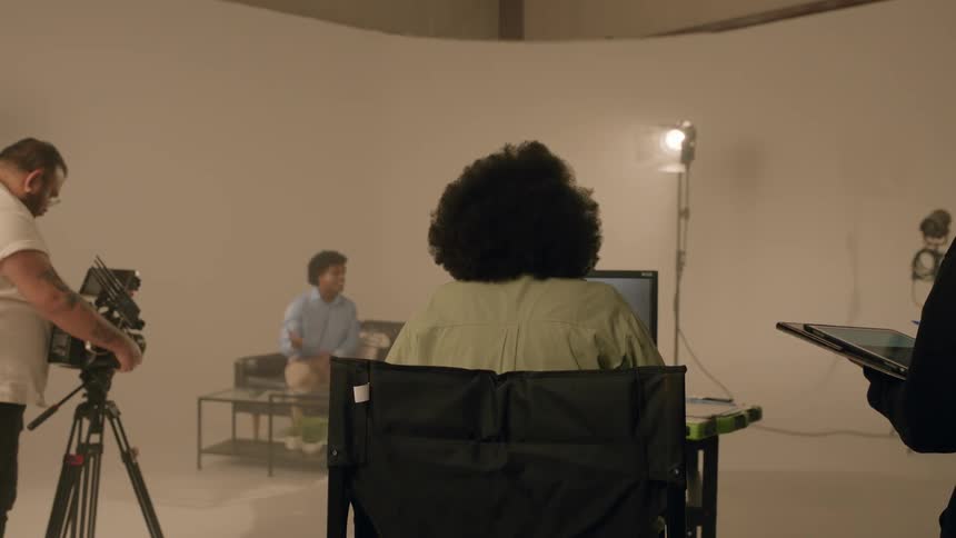 View of a woman sitting in front of a laptop inside a studio with a professional camera rolling recording