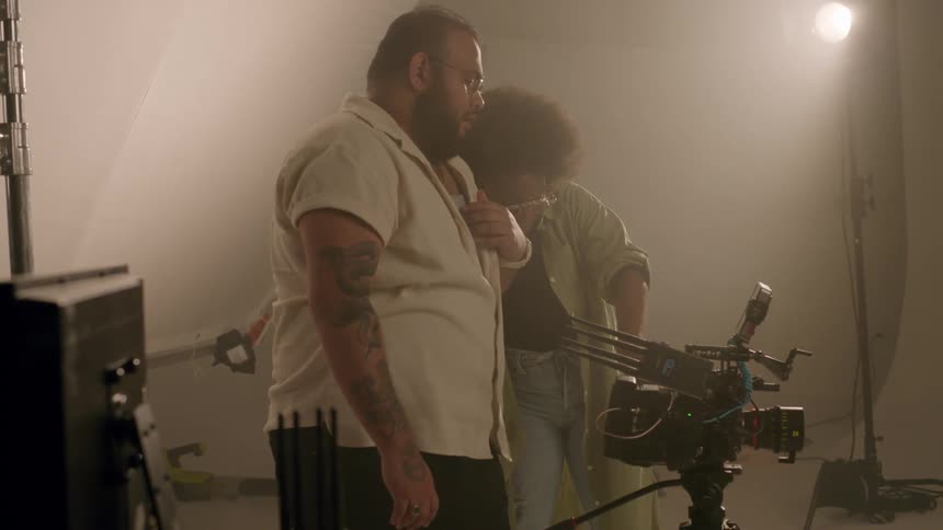 Woman next to a filmmaker adjusting the professional camera inside a studio