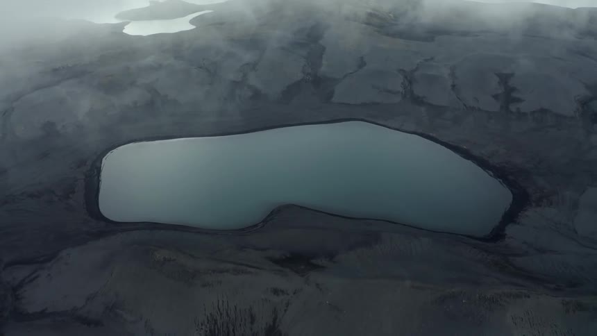 Aerial view of a crater in black rocks with a lake