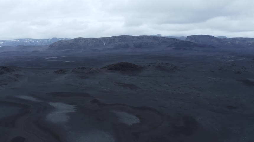 Aerial panorama of a black desert ground with hills and mountains around on a cloudy day