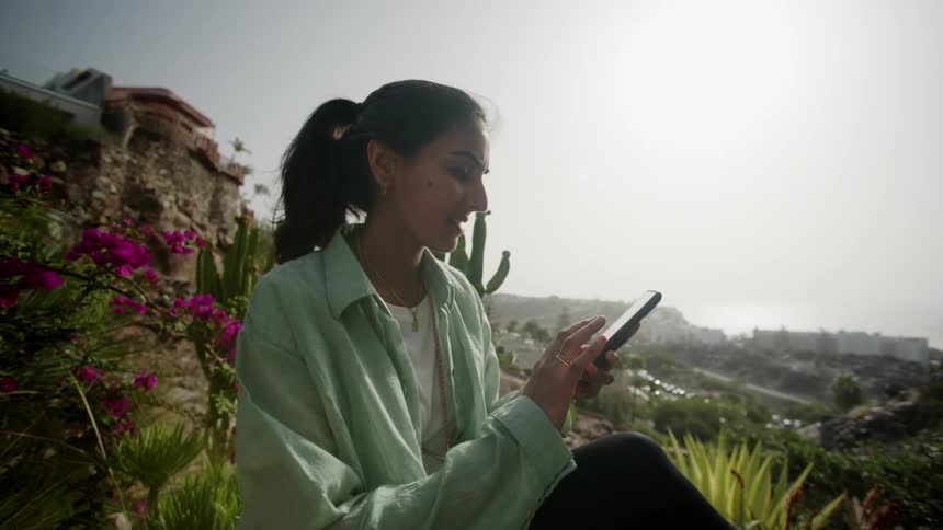 Woman texting outdoors while sitting on a deck side