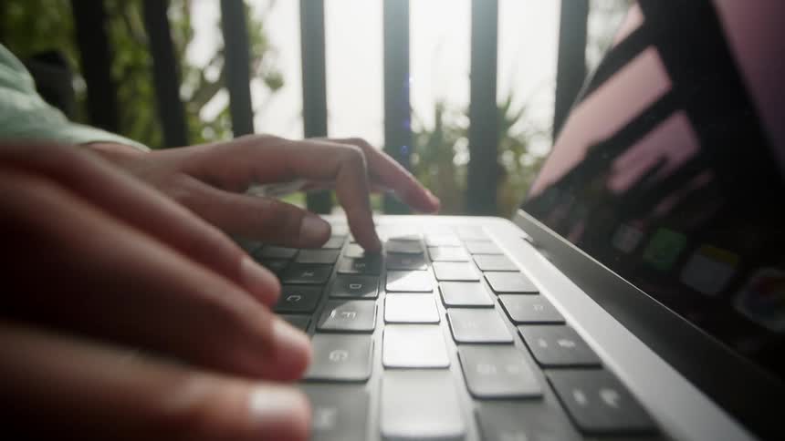 Person is typing on their laptop while sitting outdoors