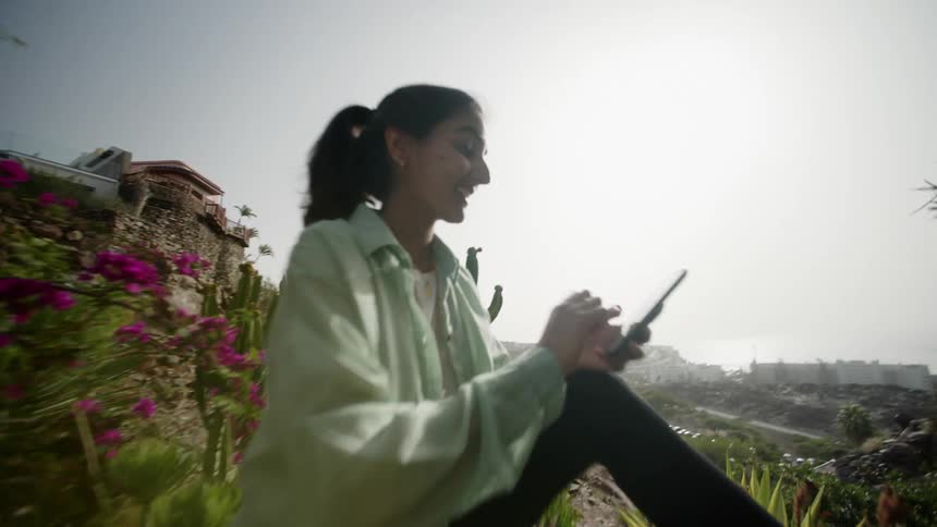 Smiling woman sitting on the balcony using her cell phone