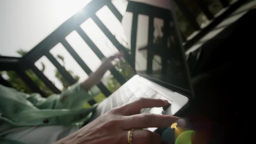 A person is folding a laptop closed outside on the deck