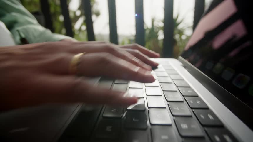 Person is sitting outdoors and typing on a laptop