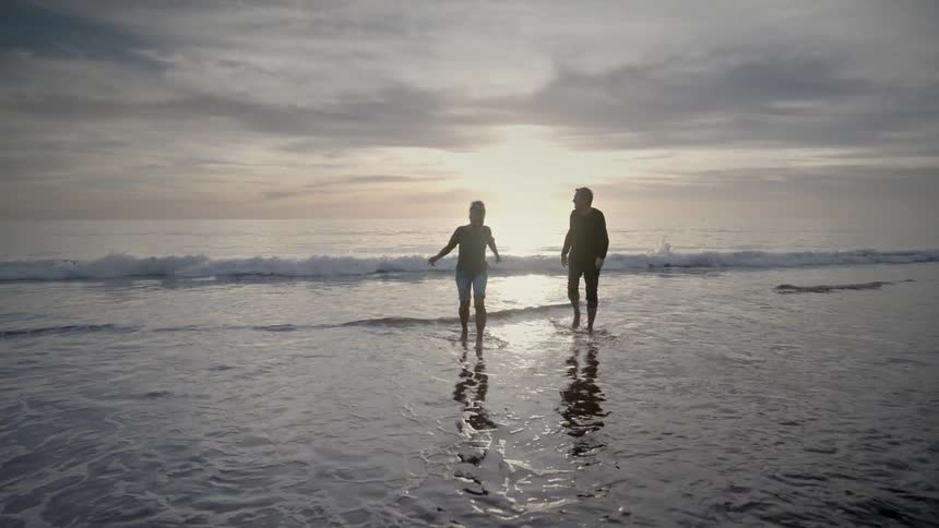 Man and woman playing in ocean water at sunset