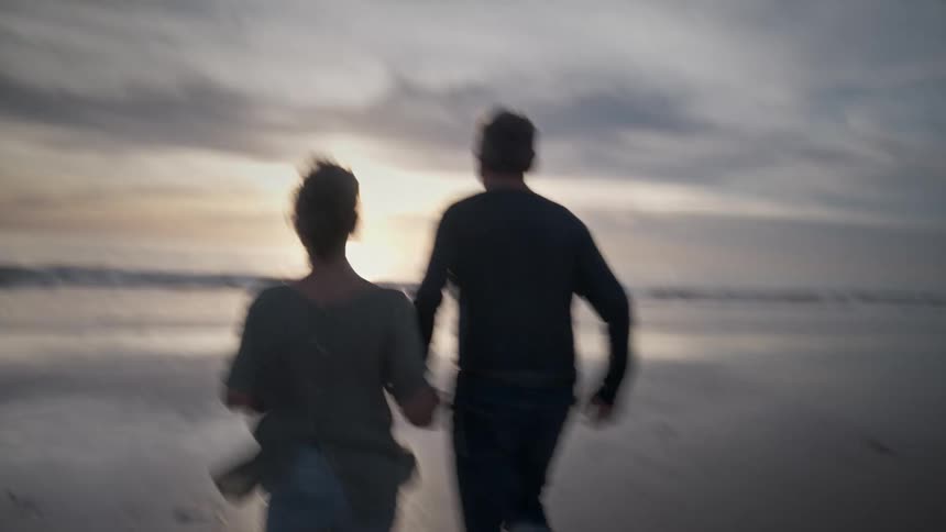 Man and woman holding hands and running on the beach