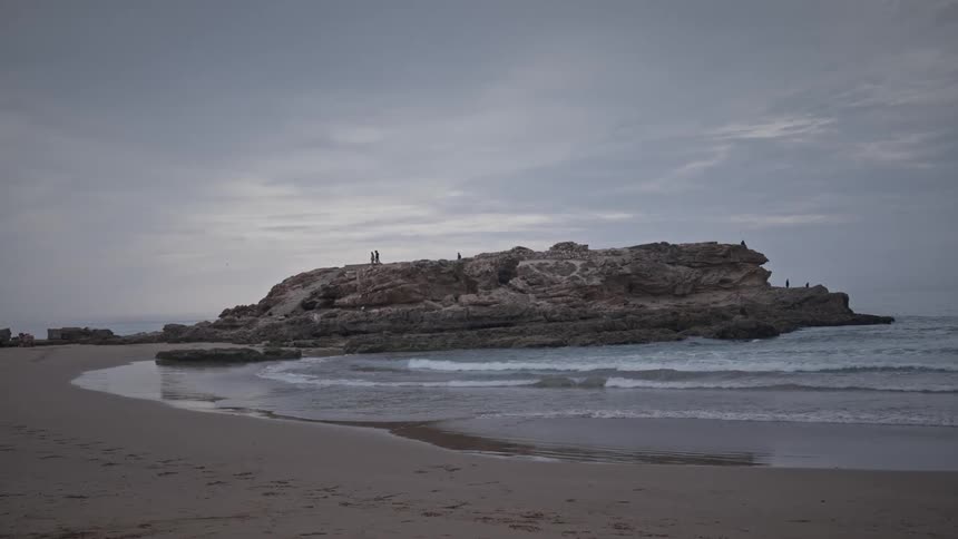 Natural scenery of a beach on a cloudy morning with the coast and a rock in the middle of the sea