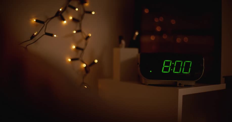 A sleeping woman reaches over to turn off an alarm clock