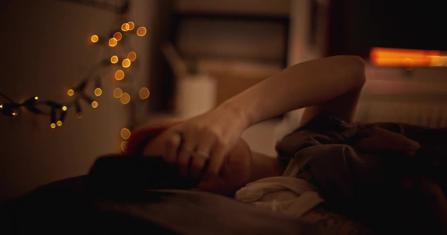 A woman is laying in bed during the night time and answering a phone call