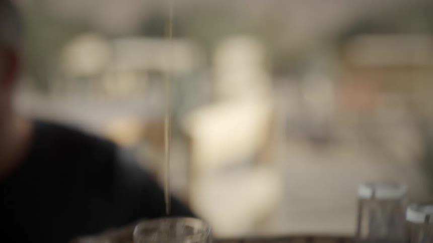 A persons hand holding a golden teapot and pouring tea into small glass cups