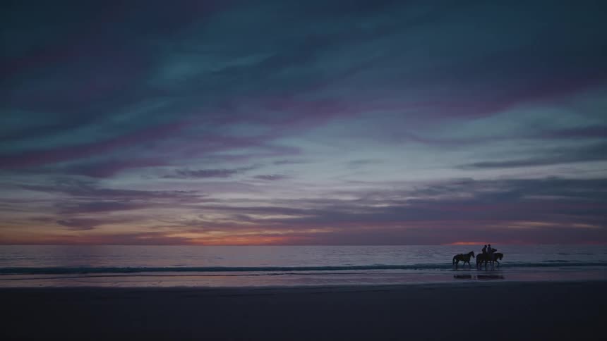 Two people riding horses along the beachfront on a sunny morning