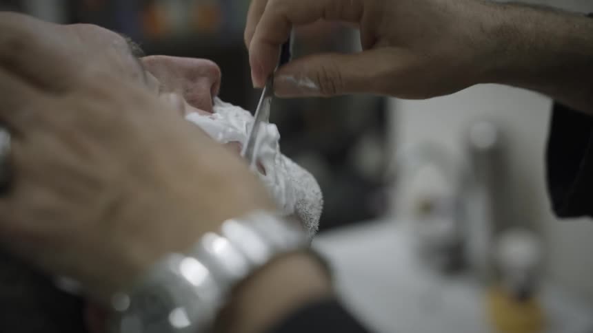 A black woman shaves a mans face