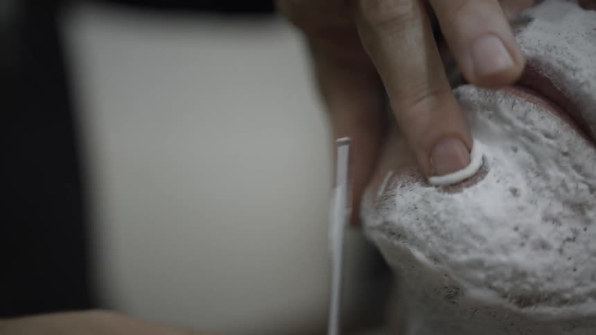 Closeup of a persons hands with a razor shaving a man