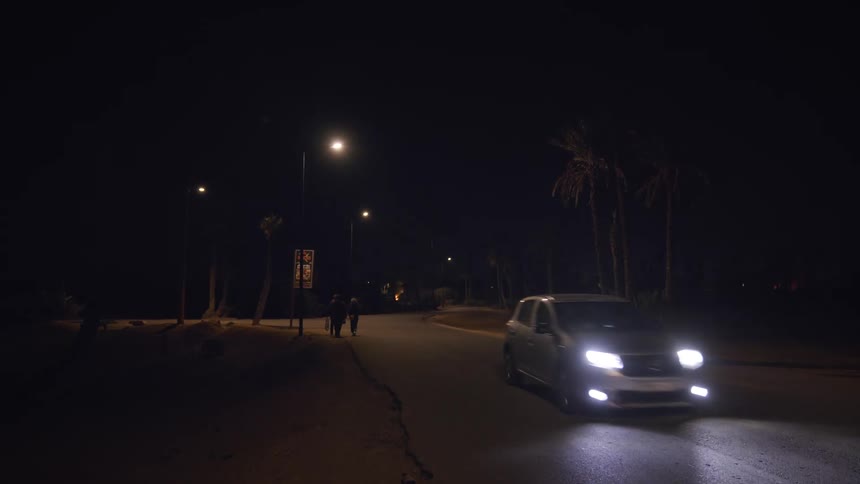 A car drives by three people walking on the road