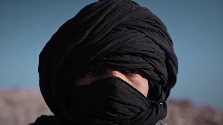 A man wearing a black turban in the desert under a clear blue sky