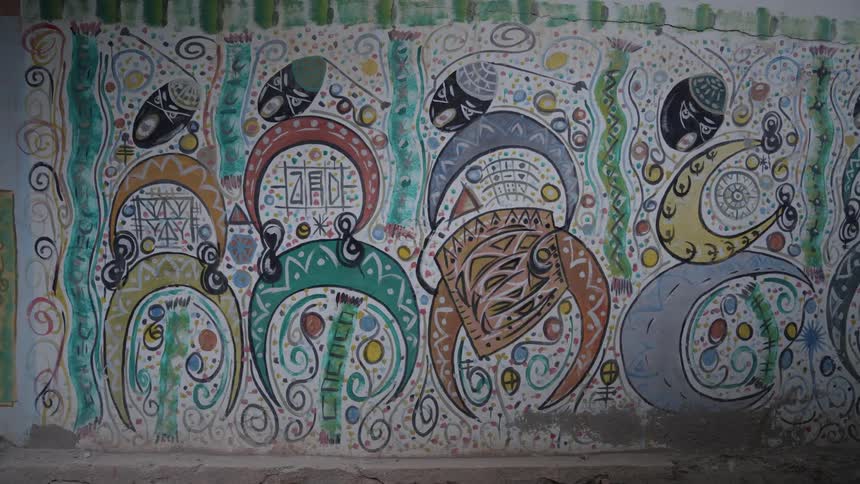Complicated colorful mural decorates exterior wall near the sidewalk during the day