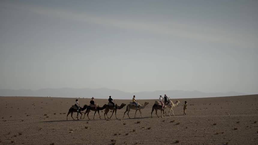 People are riding camels through the desert