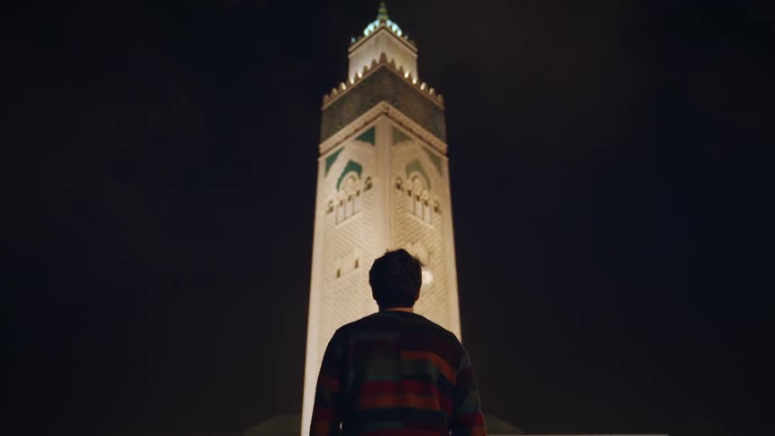 View of a man looking up at an illuminated temple tower at night