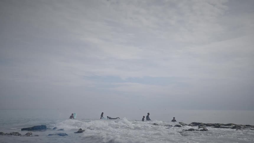 Surfers in the middle of the sea on a blue sky day with clouds