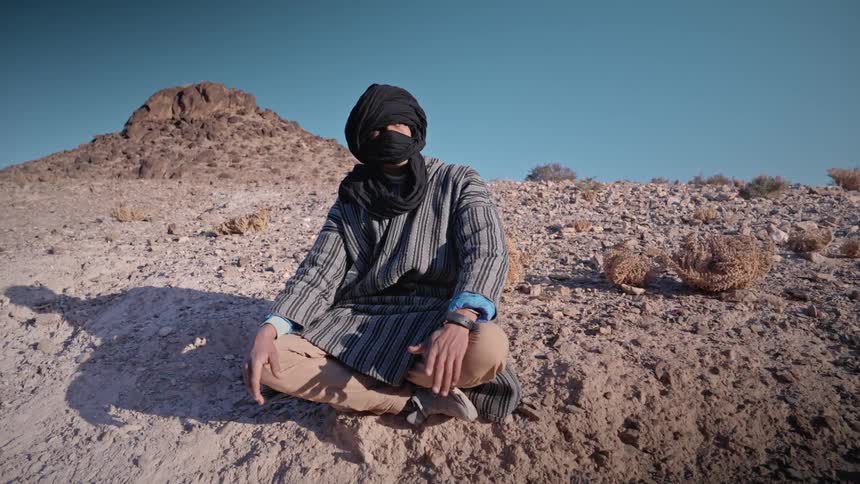 A man is sitting down in the desert sand