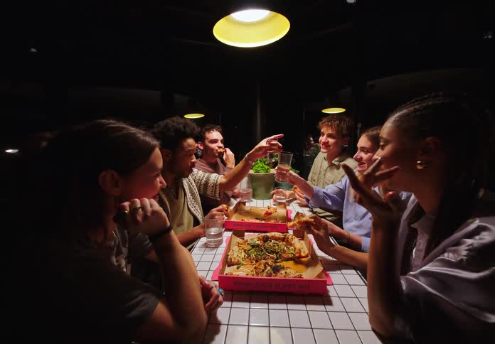 Group of friends sitting at a table toasting and eating pizza
