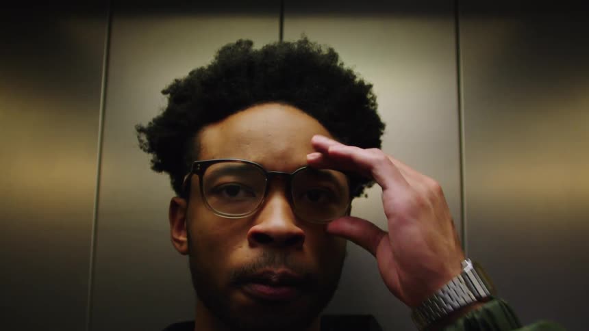A black man with closed eyes opens them and leaves an elevator