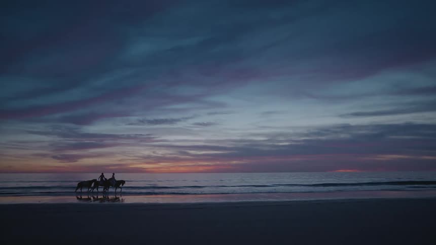 A clip of people on horses moving along the beach