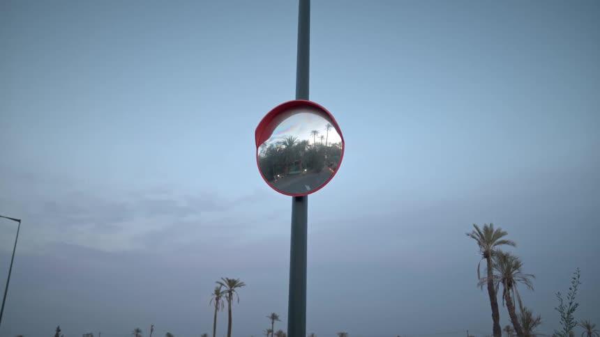 Vehicles reflected on a curved mirror over a street pole